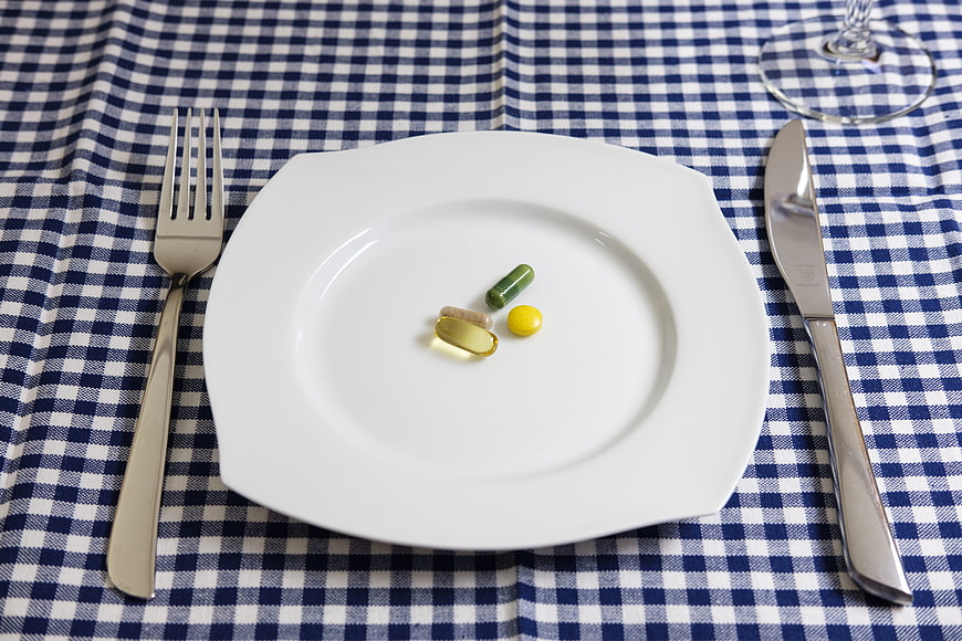 Pills on white plate with cutlery on blue checkered tablecloth