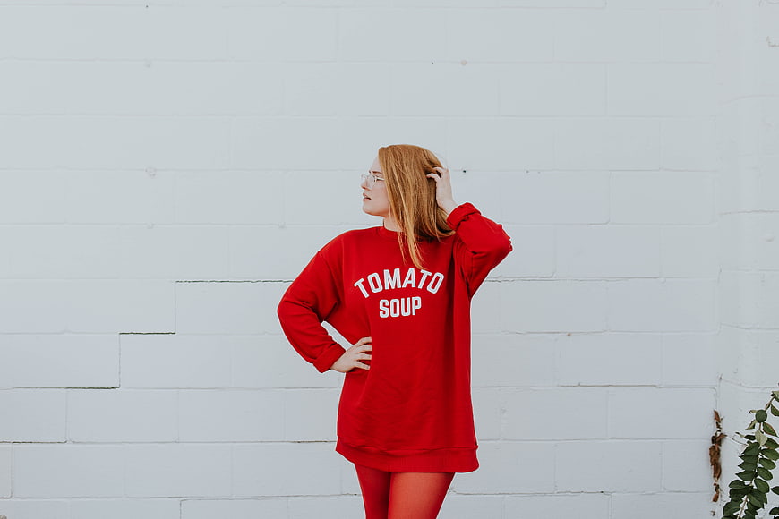 Woman in Red Tomato Soup Sweatshirt Against White Wall