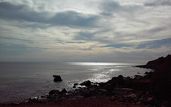 Dramatic cloudy seascape with rocky shoreline and distant sailboat