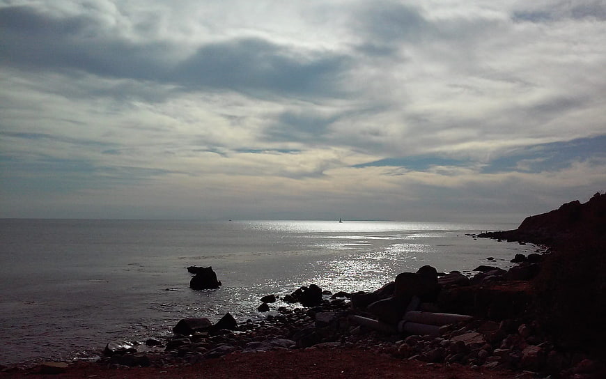 Dramatic cloudy seascape with rocky shoreline and distant sailboat
