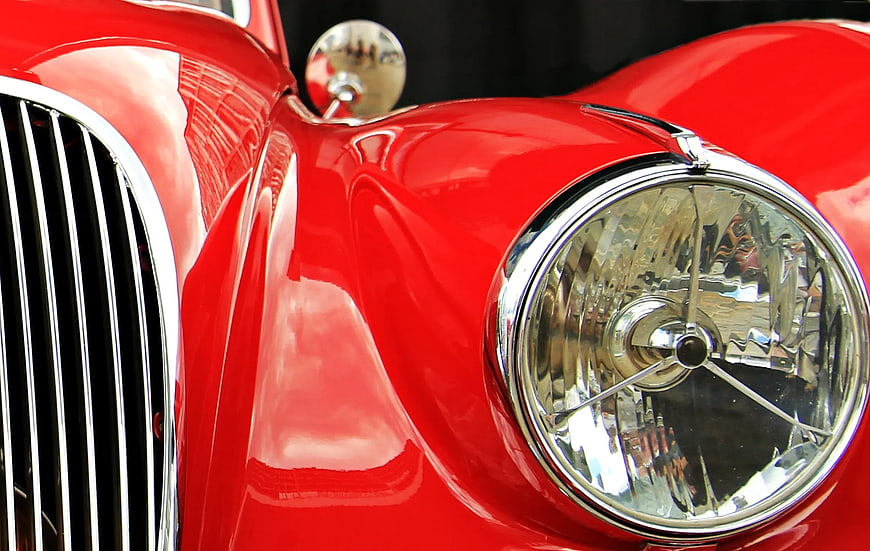 Close-up of vintage red car headlight and chrome grille