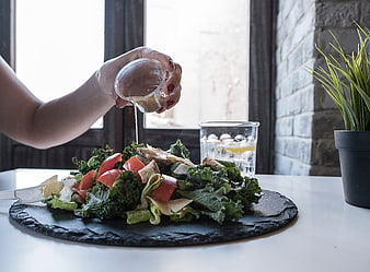 Woman pouring dressing on fresh kale salad with tomatoes