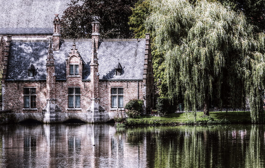 Historic brick canal house in Bruges with weeping willow reflection