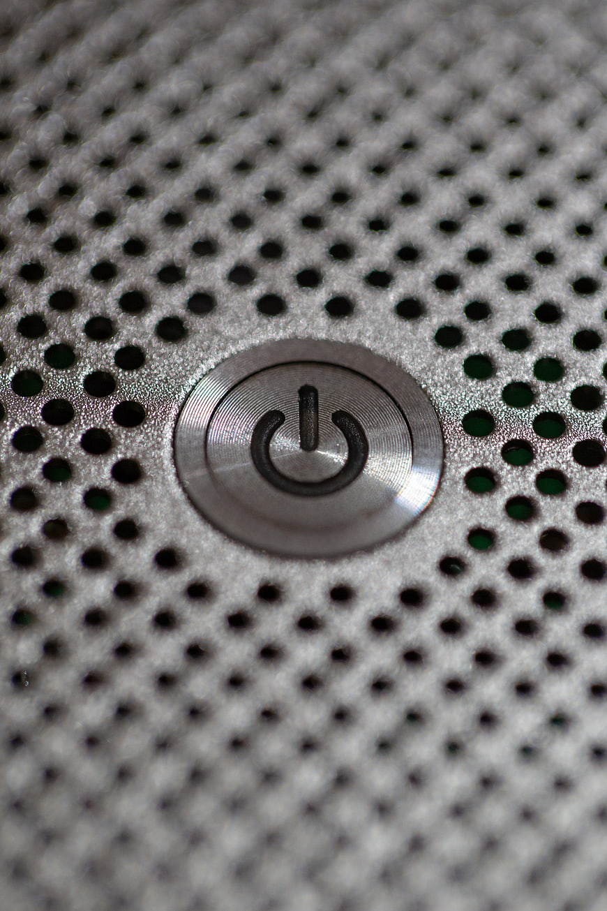 Close-up of a silver power button on a perforated metal surface