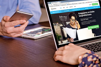 Person using smartphone and laptop with accounting website on screen