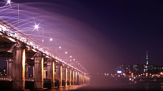 Nighttime cityscape with illuminated bridge and distant tower