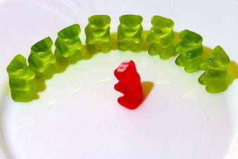 Red Gummy Bear Surrounded by Green Gummy Bears on White Plate