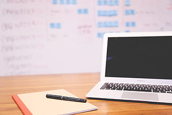 Laptop and notebook on wooden desk with whiteboard background
