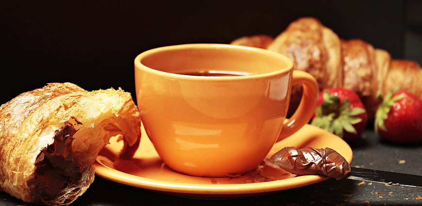 Orange coffee cup with chocolate croissant and strawberries