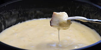 Melted cheese fondue dripping from bread on a fork