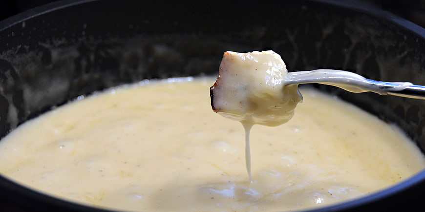 Melted cheese fondue dripping from bread on a fork