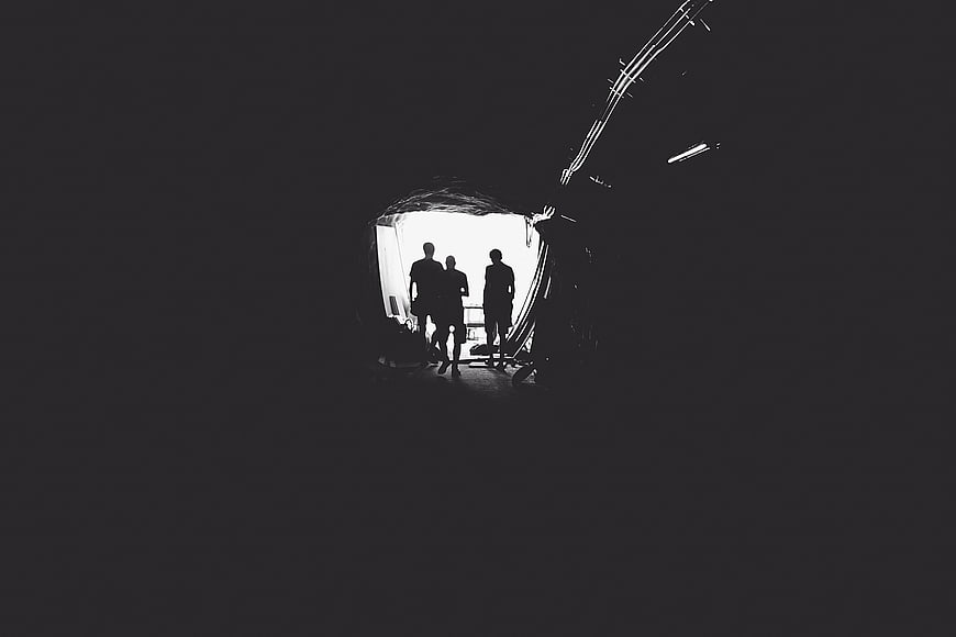 Silhouettes of three people standing in a dark tunnel entrance