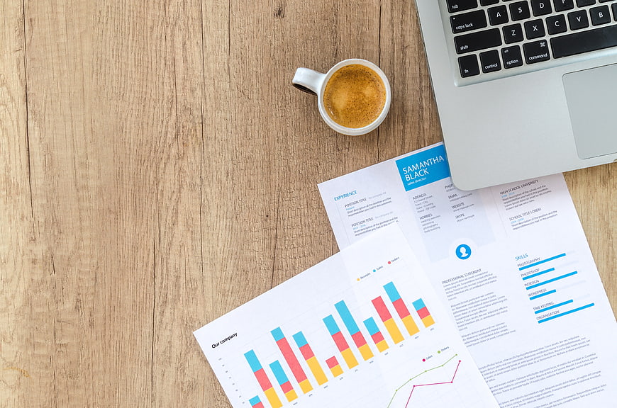 Flat lay of business documents, laptop, and coffee on wooden desk