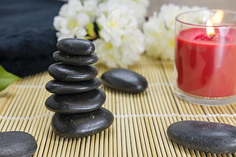 Stacked black zen stones with red candle and white flowers on bamboo mat