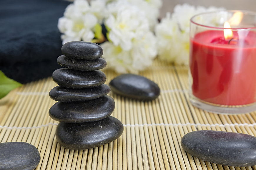 Stacked black zen stones with red candle and white flowers on bamboo mat
