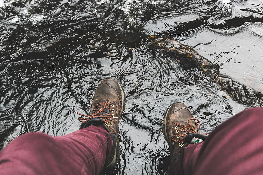 First-person view of hiking boots dangling over rushing river water
