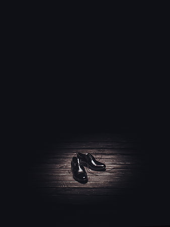 Black leather shoes on dark wooden floor with dramatic lighting