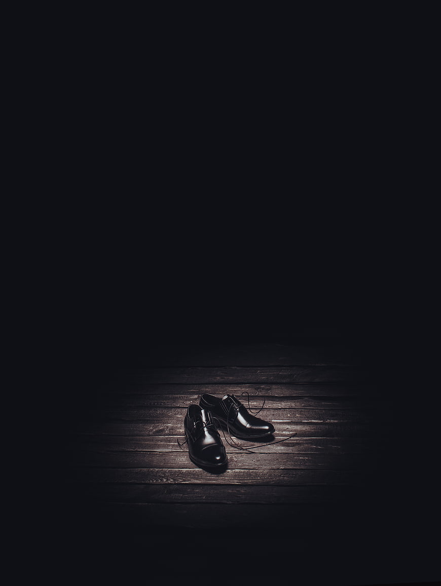 Black leather shoes on dark wooden floor with dramatic lighting