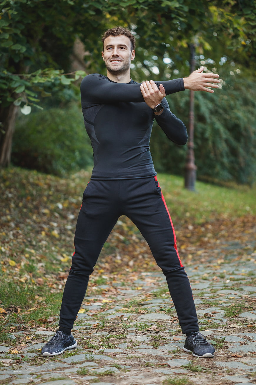 Smiling Man Stretching Arms in Autumn Park