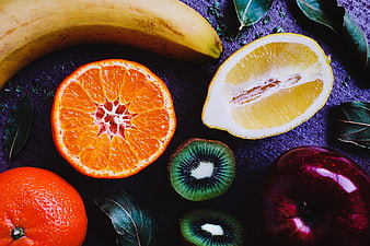 Flat lay of fresh sliced citrus fruits, kiwi, and apple on dark background