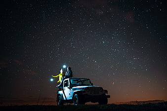 Couple stargazing from jeep under starry night sky