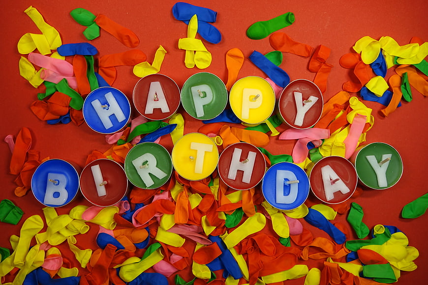Happy Birthday Candles and Deflated Balloons on Red Background