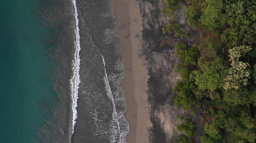 Aerial View of Turquoise Ocean Waves Meeting Sandy Beach and Forest