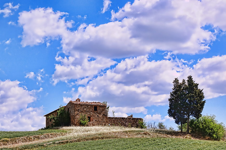 Rustic stone farmhouse on a grassy hill under a blue sky
