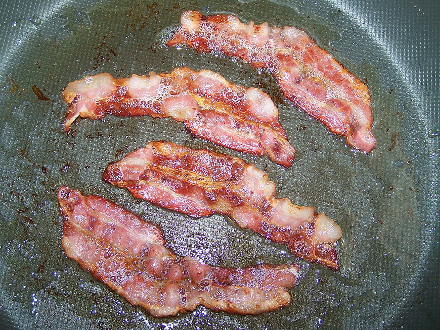Sizzling bacon strips frying in a pan