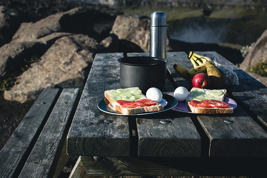 Healthy camping breakfast with sandwiches and fruit on wooden table