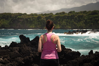 Woman in Pink Top Looking at Ocean from Rocky Coast