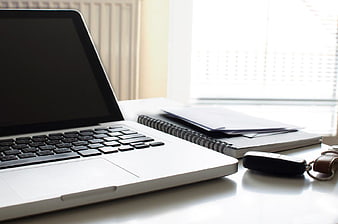 Laptop, car keys, and notebook on a bright office desk