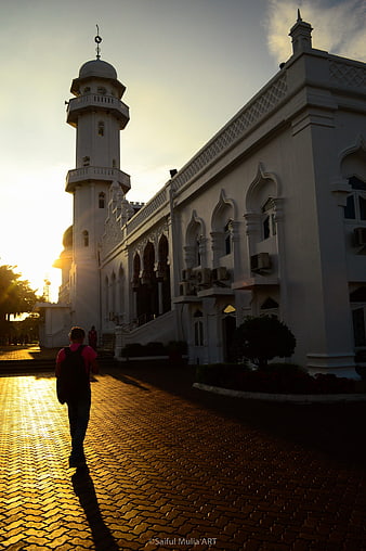 Man walking past white mosque at golden hour