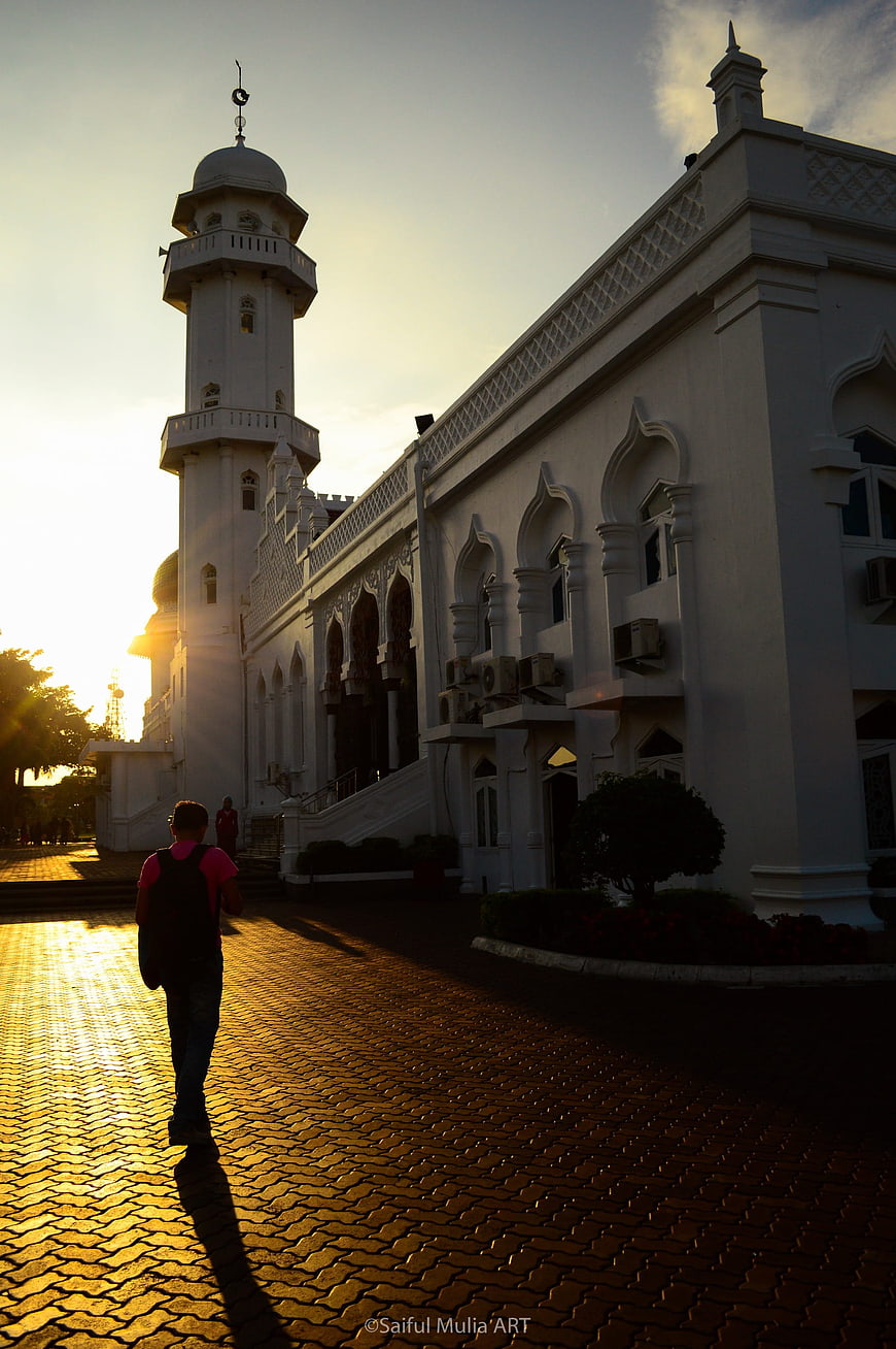 Man walking past white mosque at golden hour