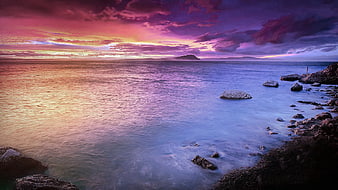 Vibrant purple and pink sunset over calm ocean with rocky shore