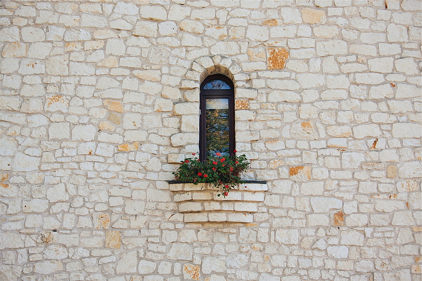 Arched window with red flowers on white stone wall