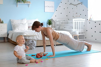 Mother doing yoga plank while baby plays with blocks