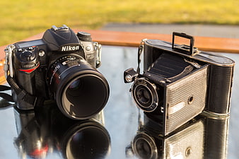 Modern Nikon DSLR and vintage folding camera on glass table
