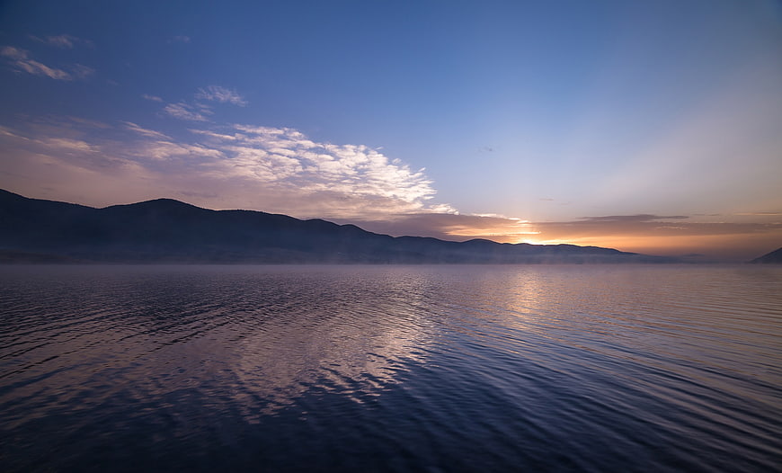 Serene Lake Sunrise with Misty Mountains and Blue Sky