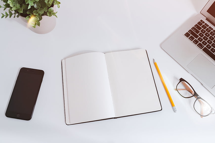 Minimalist white desk workspace with open notebook and laptop