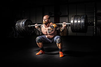Muscular tattooed man performing heavy barbell squat in dark gym