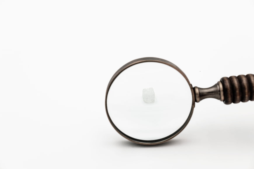 Antique magnifying glass focusing on a single small sugar cube on white background