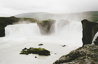 Misty waterfall cascading over mossy rocks in a rugged landscape