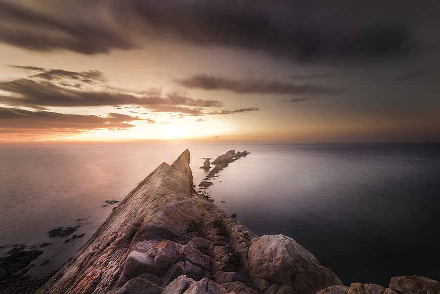 Dramatic Rocky Headland Leading Into Calm Ocean At Sunset