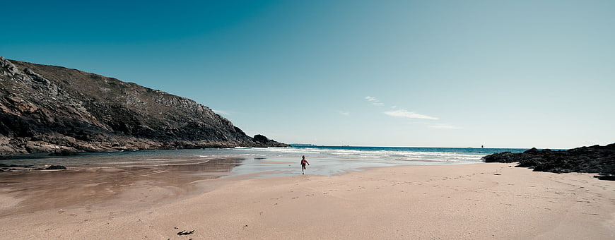 Lone figure walking on sandy beach near rocky cliffs