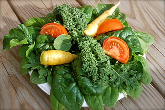 Fresh vegetable salad with spinach, kale, tomatoes, and yellow carrots on a wooden table