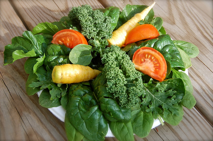 Fresh vegetable salad with spinach, kale, tomatoes, and yellow carrots on a wooden table