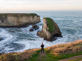 Man standing on cliff overlooking dramatic ocean sea stack