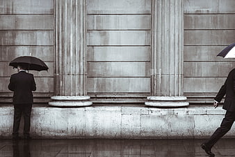 Two Men with Umbrellas Walking Past Classical Columns in Rain