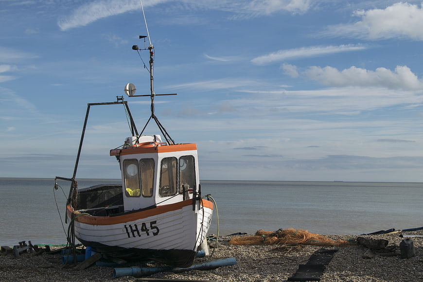White and orange fishing boat resting on pebble beach